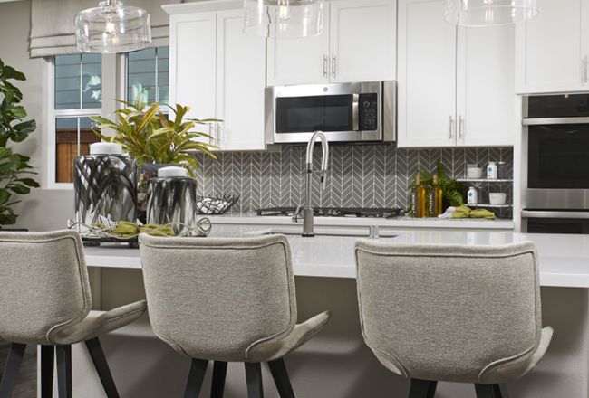 Kitchen island with three chairs, overlooking gray and white chevron tile backsplash