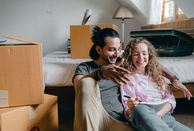 Couple sitting on floor surrounded by moving boxes, making a moving checklist