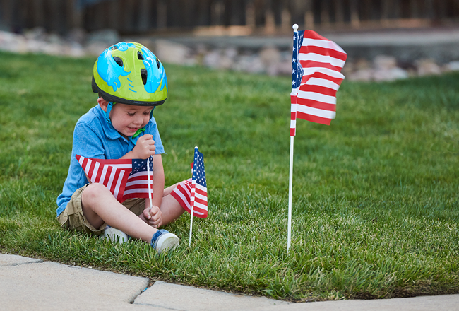 Boy wearing helmet, placing small American flag in the lawn
