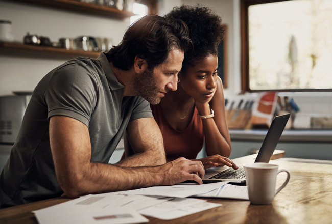 Couple sitting at kitchen table shopping for home insurance on a computer