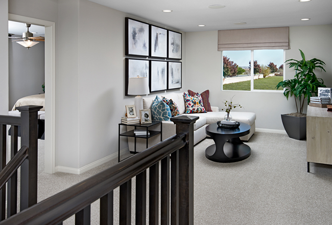 Upper floor open room that you enter right from the staircase, straight ahead there is a large window, to the left of the window is a 'L' shaped couch, along with a side table, and coffee table touching the couch. Across from the couch is a tv stand