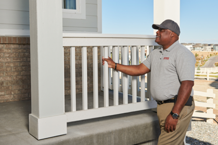 Man inspecting a home exterior, with his hand on the front porch railing