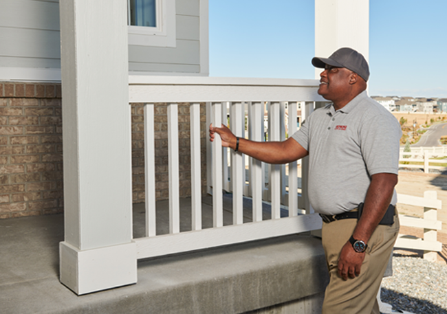 Man inspecting a home exterior, with his hand on the front porch railing