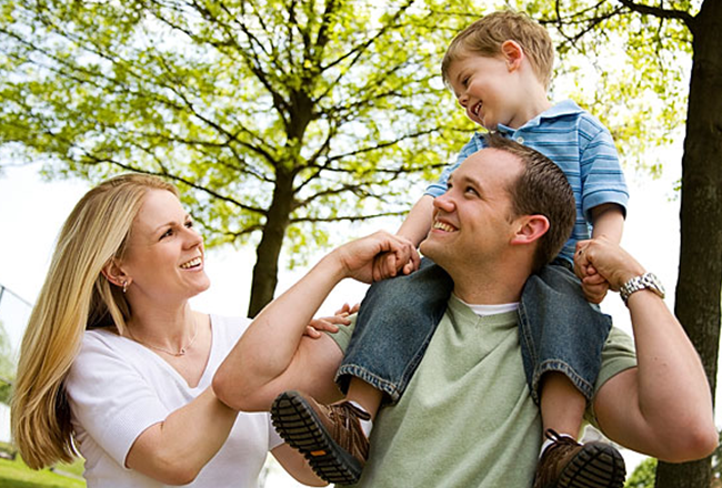 Woman and man with young son on his shoulders, smiling outside