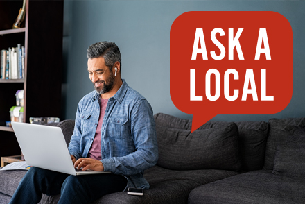 Man sitting on couch at home with laptop on his lap and wireless earbud in his ear
