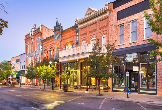 A street view of restaurants and shops on Main Street in Columbia. The buildings are built with brick and there is street parking, bike racks, and trees outside of the shops