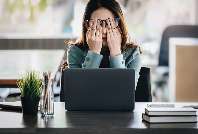 Woman at a laptop, pressing her hands over her eyes in apparent frustration