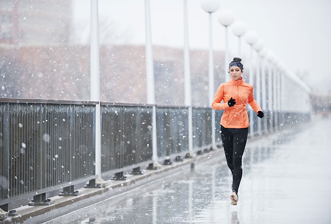 Woman jogging on a sidewalk while snow falls
