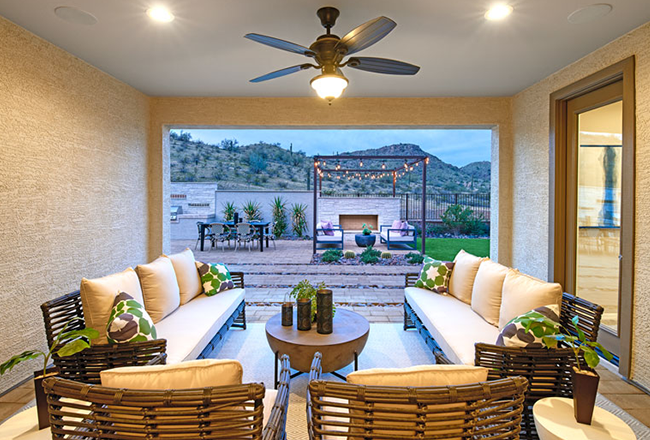 Room with lounge chairs and couches with open wall towards backyard with large patio, outdoor kitchen, dining table, lounge chairs, and a fireplace.