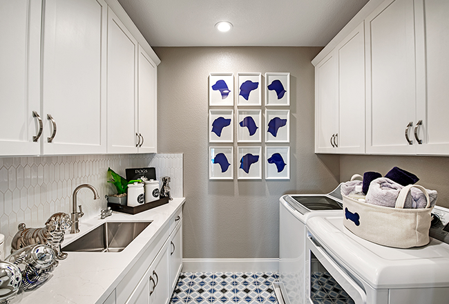 Laundry room with upper and lower cabinets, long countertop with large sink on one side, and washer and dryer and upper cabinets on the opposite wall.