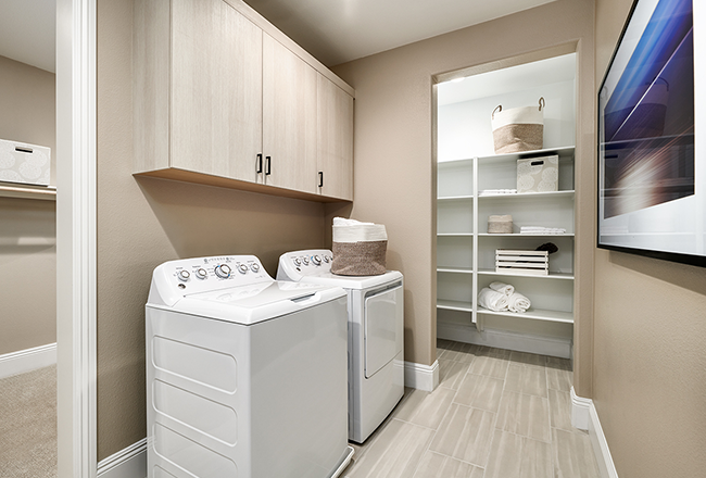Washer and dryer with cabinets above, next to doorway with built-in shelves.