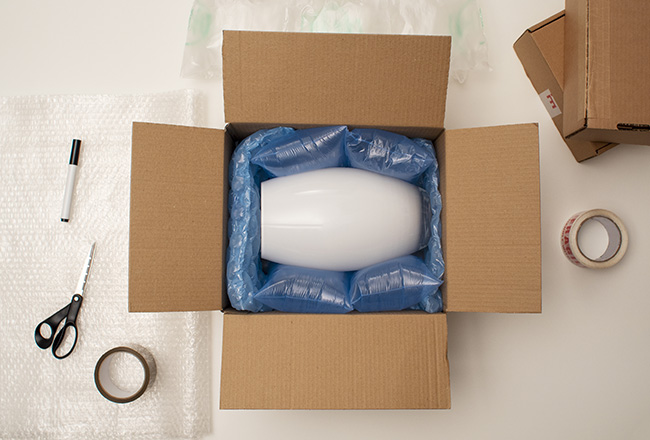 Vase surrounded by bubble wrap in a cardboard box, with packing supplies all around