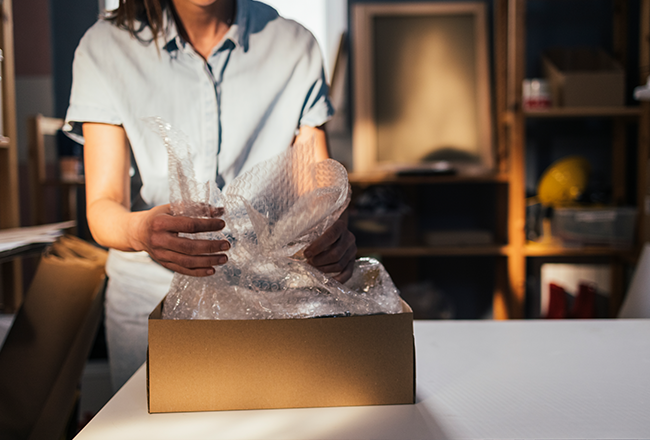 Woman wrapping dishes in bubble wrap and packing them in a box