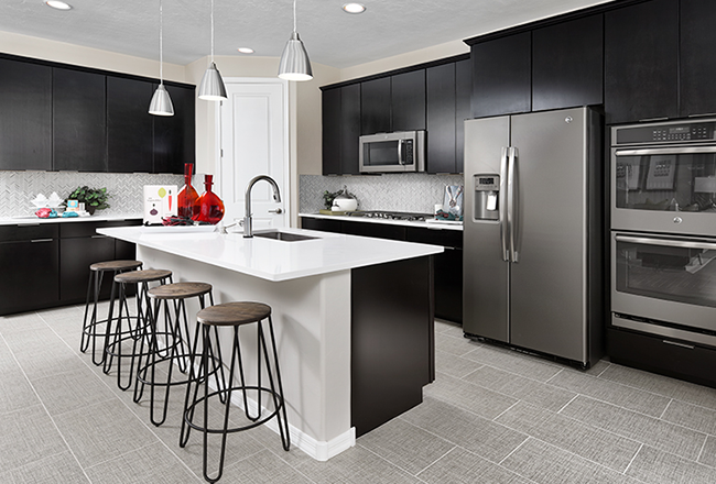 Kitchen with large island with four bar stools, pantry door, gas stove, microwave, two ovens, and refrigerator.