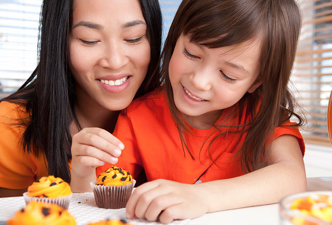 Mother and daughter decorating Halloween-themed cupcakes