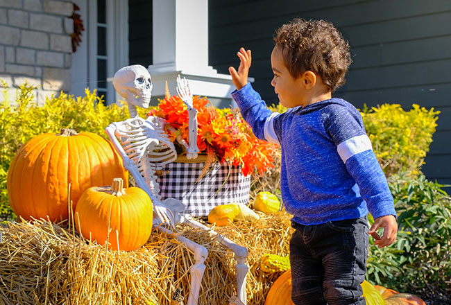 Young boy high-fiving a fake skeleton Halloween decoration on a front porch