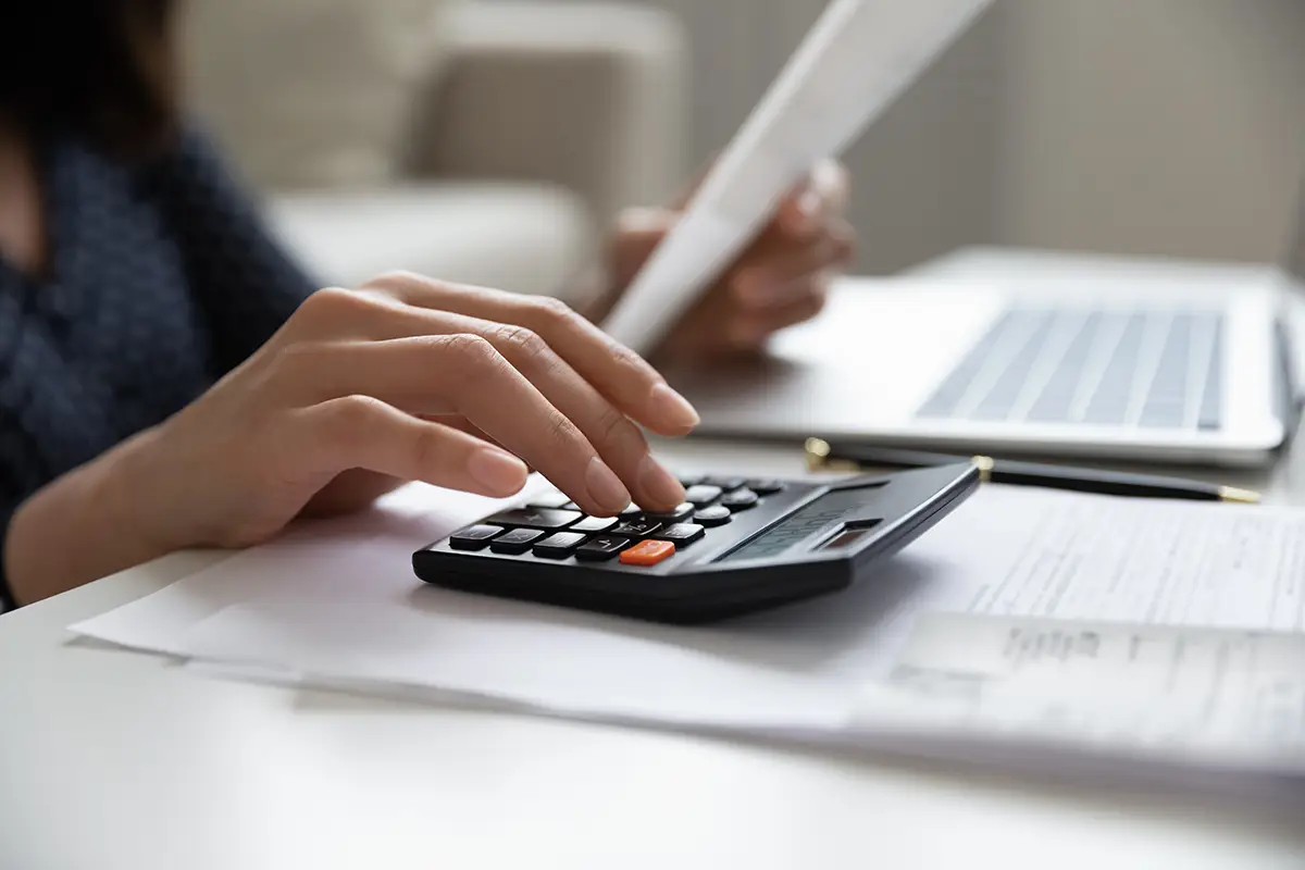 Woman typing on a calculator and looking at paperwork for creative ways to save money.