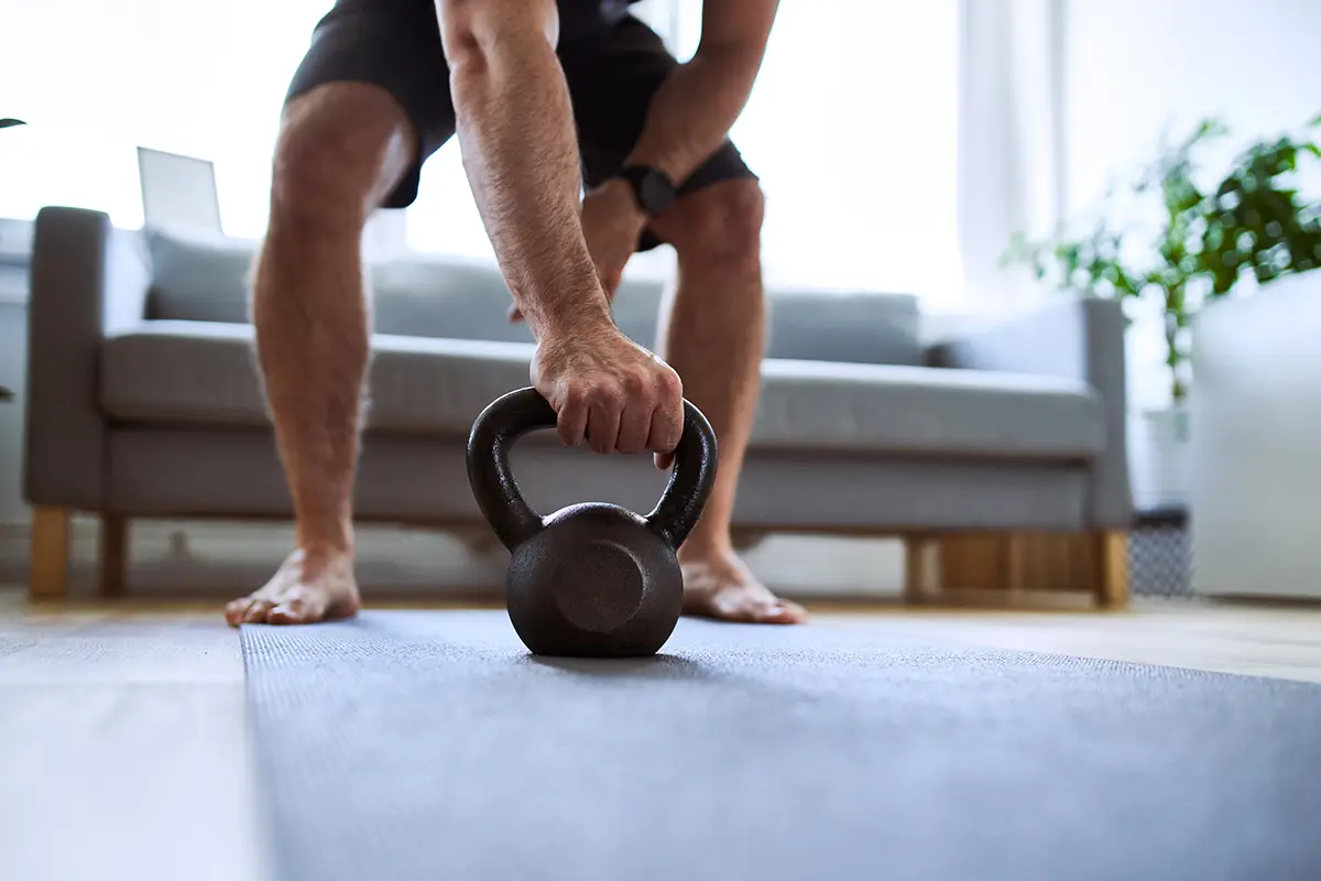 Man lifting kettle bell off home gym floor.