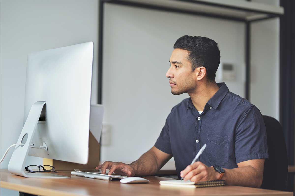 Man browsing home listings on his computer, writing down information.