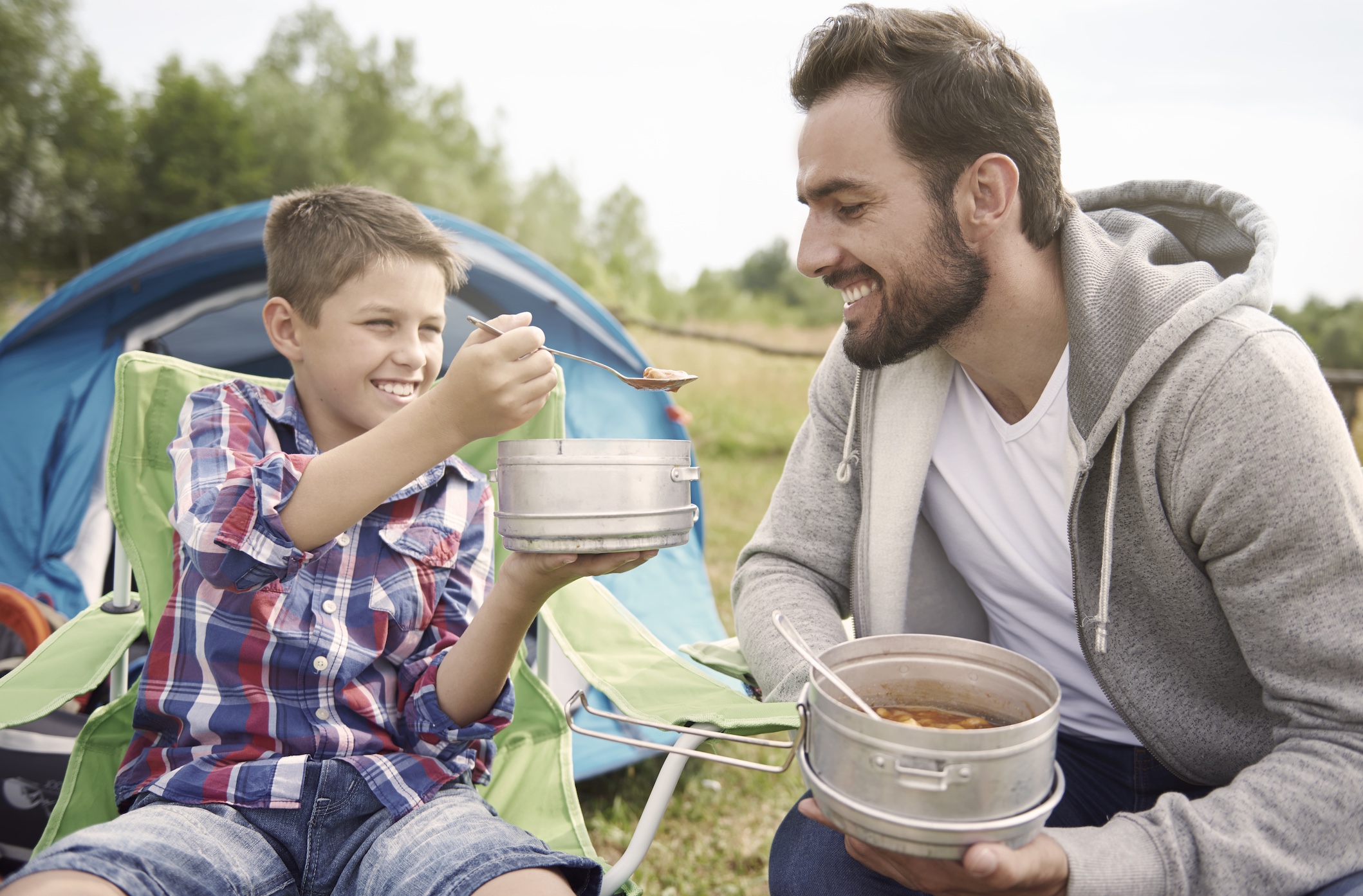 Father and son sharing soup at a campsite