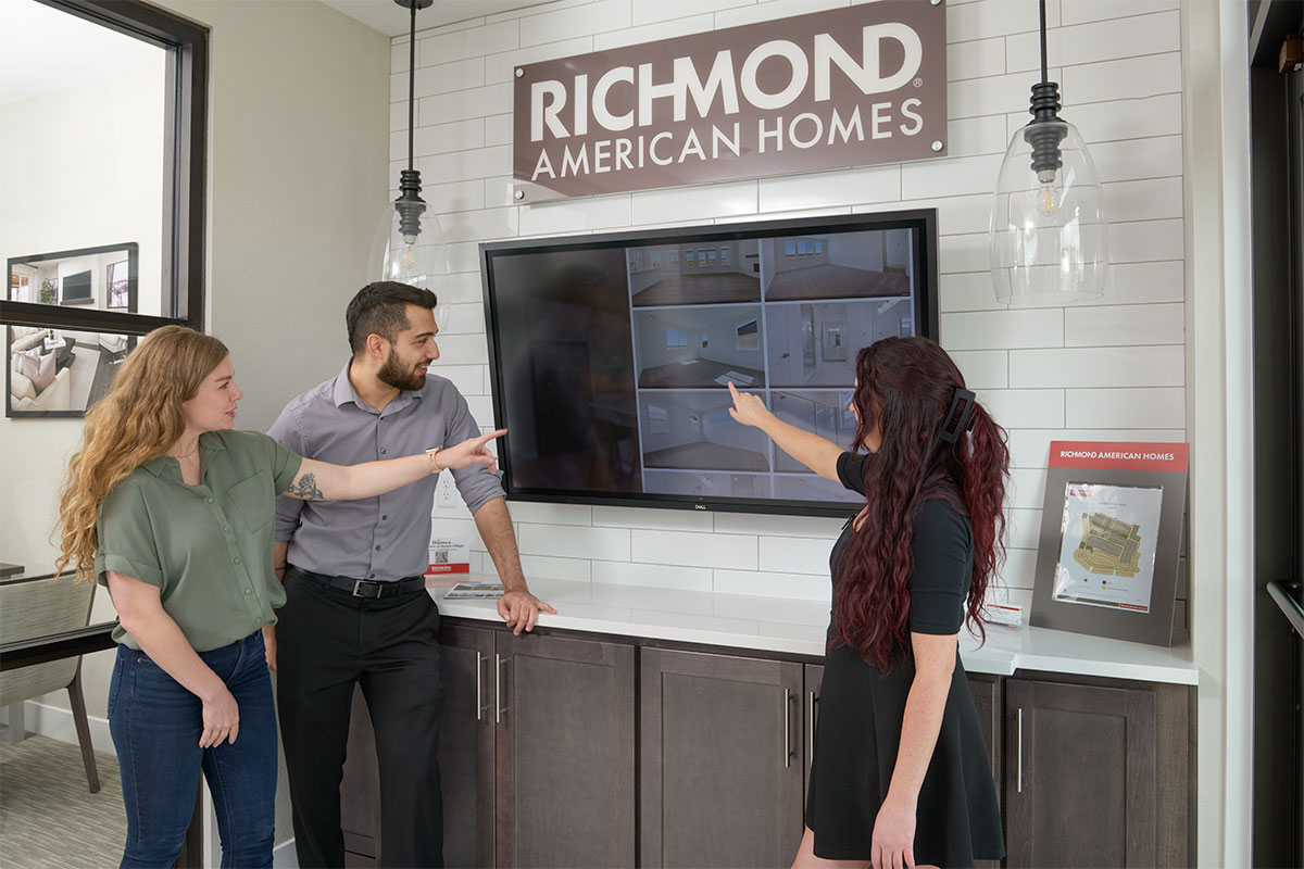 A young couple and a sales associate looking and pointing at images of listings on a screen in the Sales Center