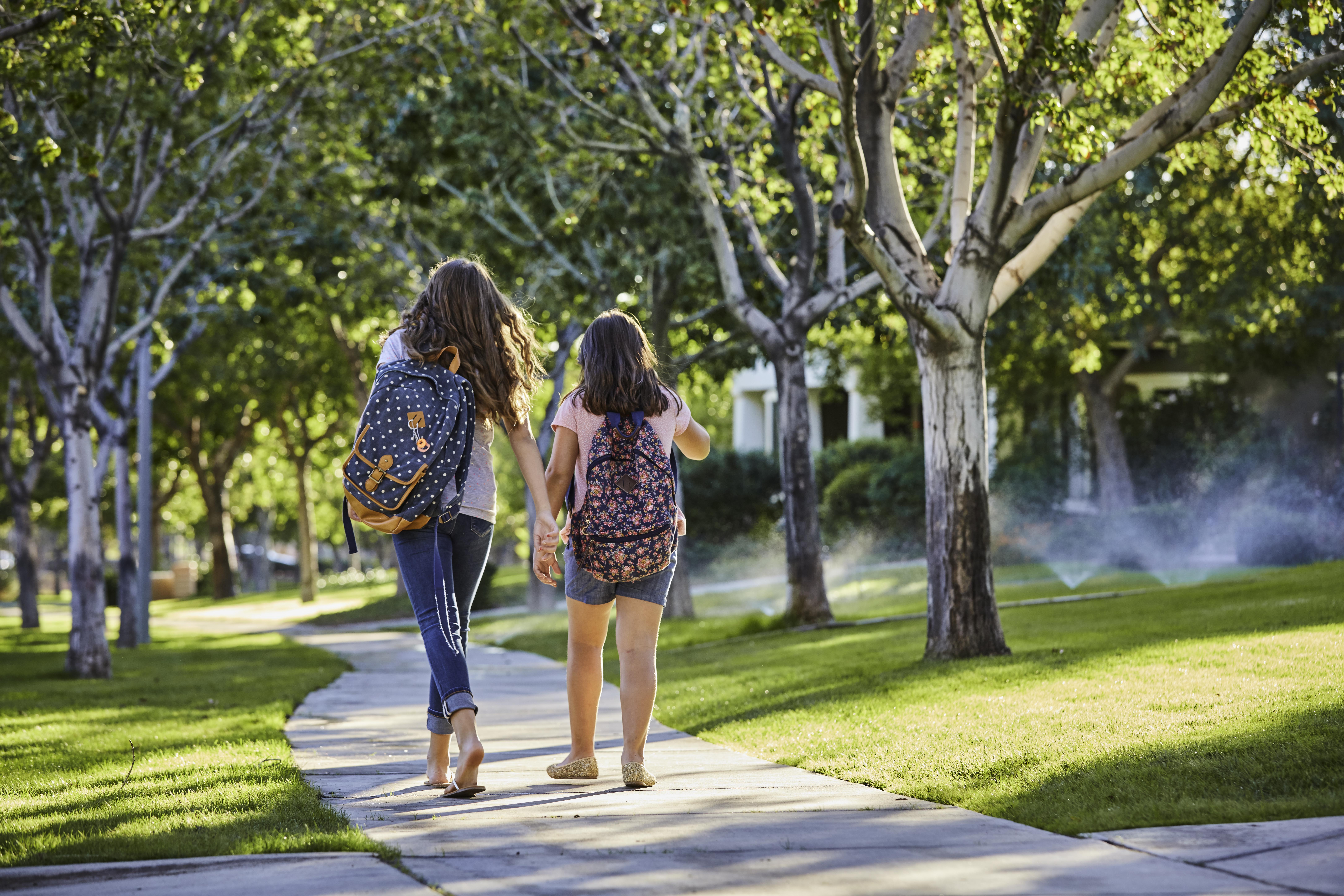 Two kids wearing backpacks and walking through a neighborhood