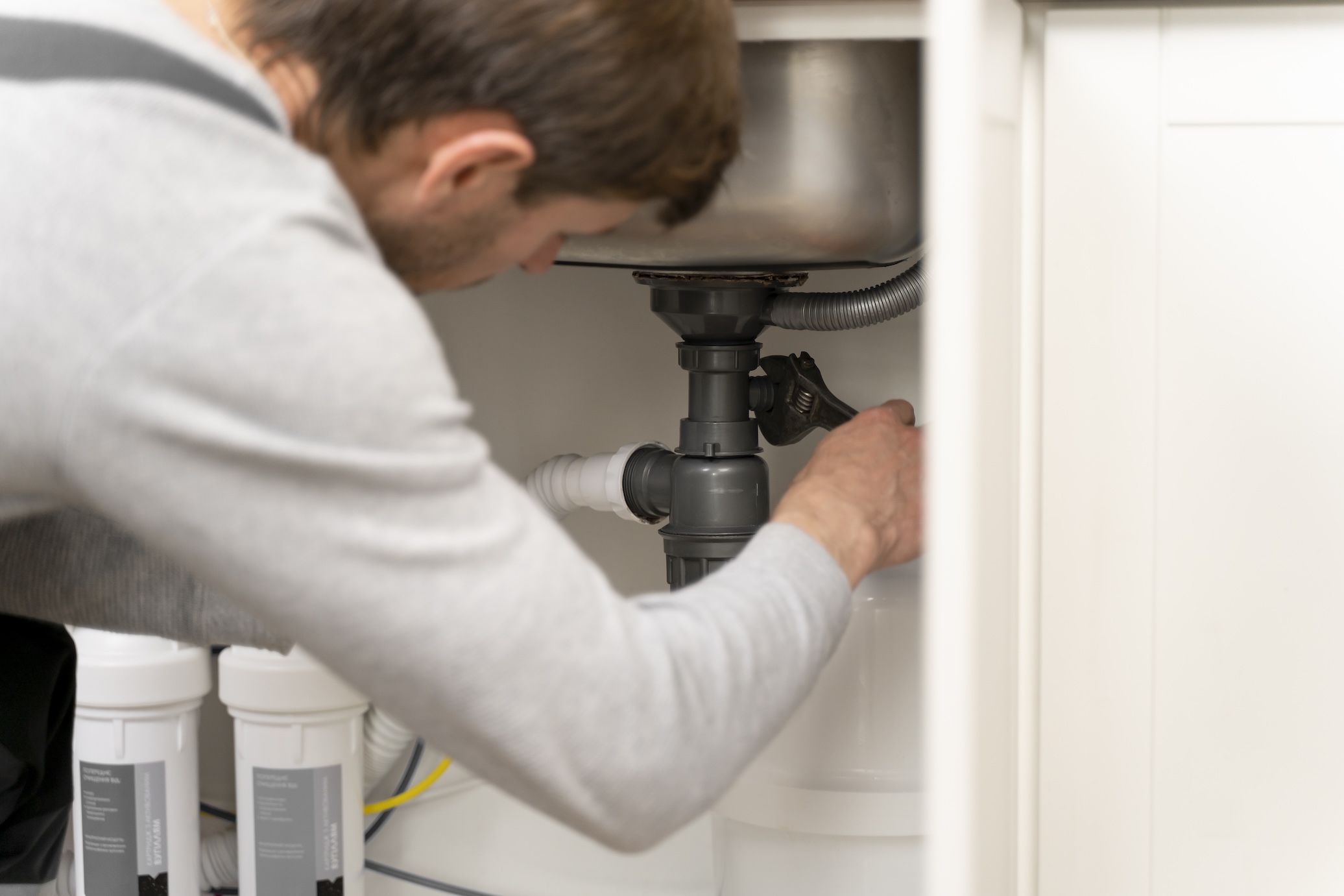 A plumber working on the pipes below a sink