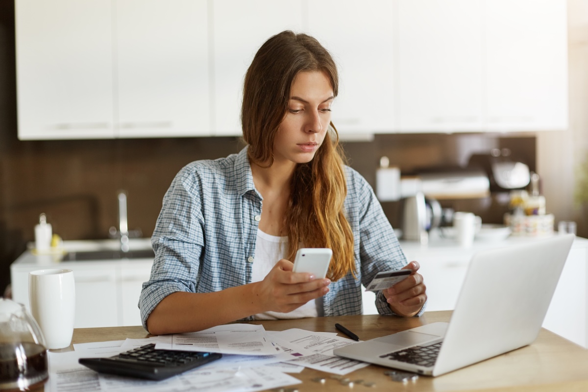 A woman looking at a laptop and holding her credit card and her phone