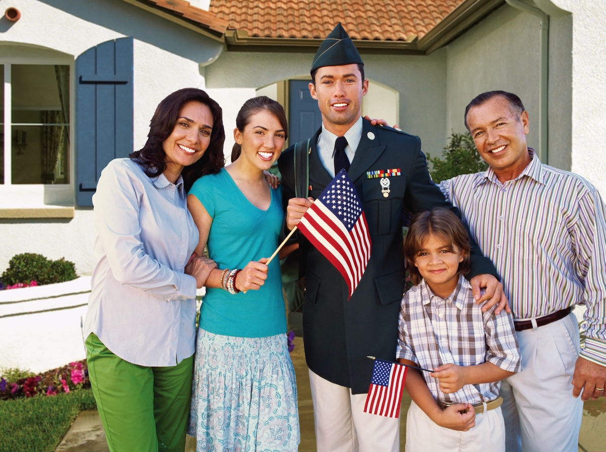 A smiling family holding American flags and hugging a young man in a military uniform