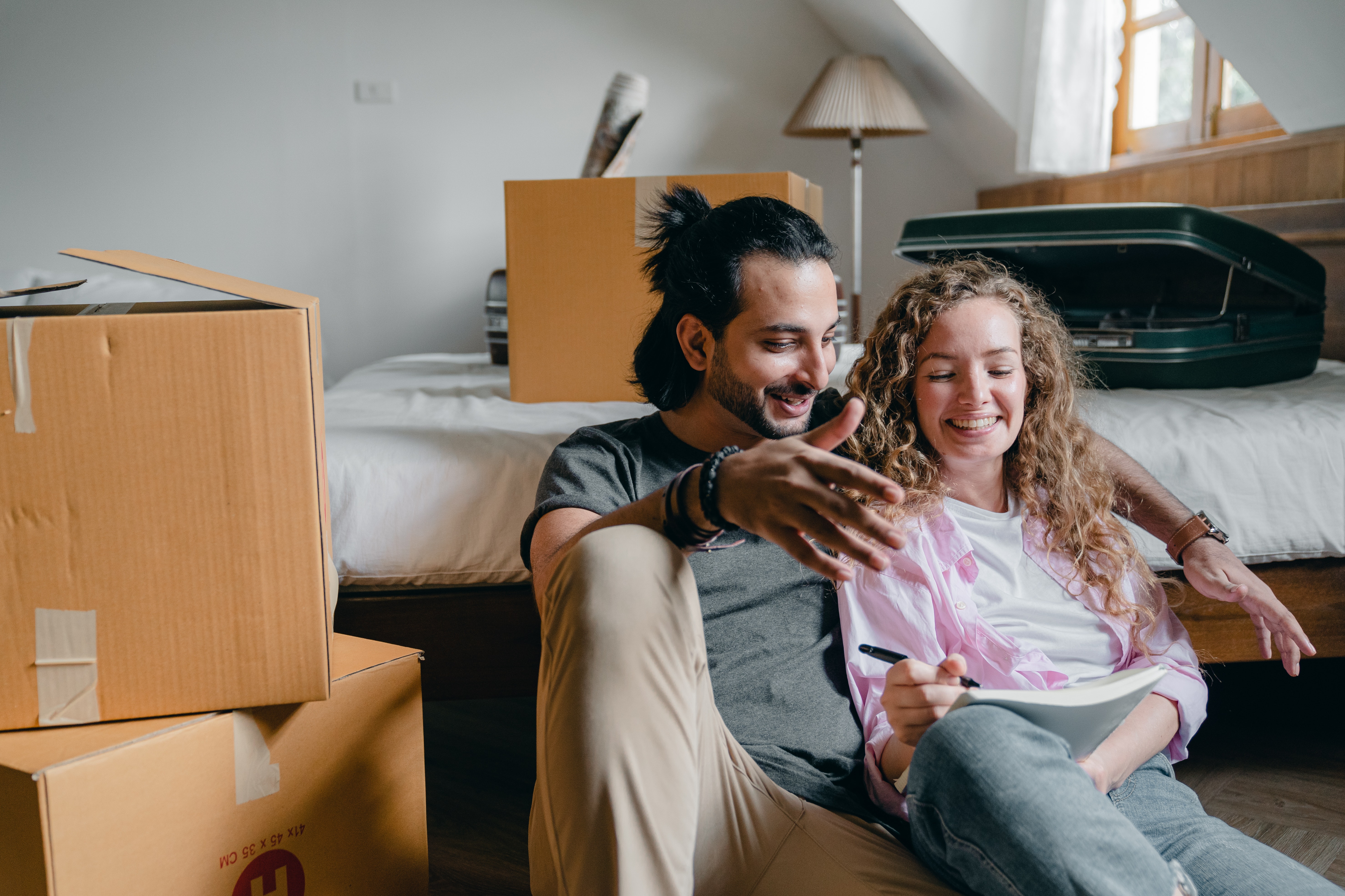 A couple sitting on the floor of their new room, surrounded by moving boxes
