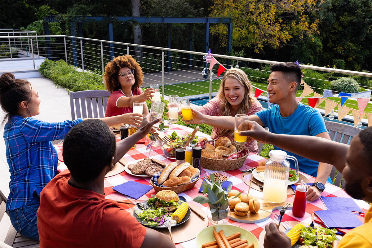 friends clinking glasses over a backyard picnic