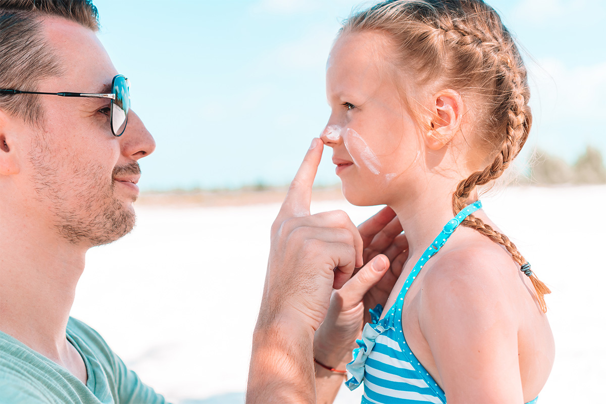 father applying sunscreen on daughter's nose