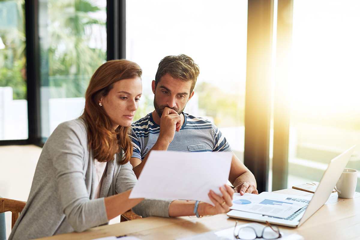 Couple, finance and budget conversation with documents planning for tax, bills and savings on laptop with banking, online payment and investment. People, financial thinking and household strategy.