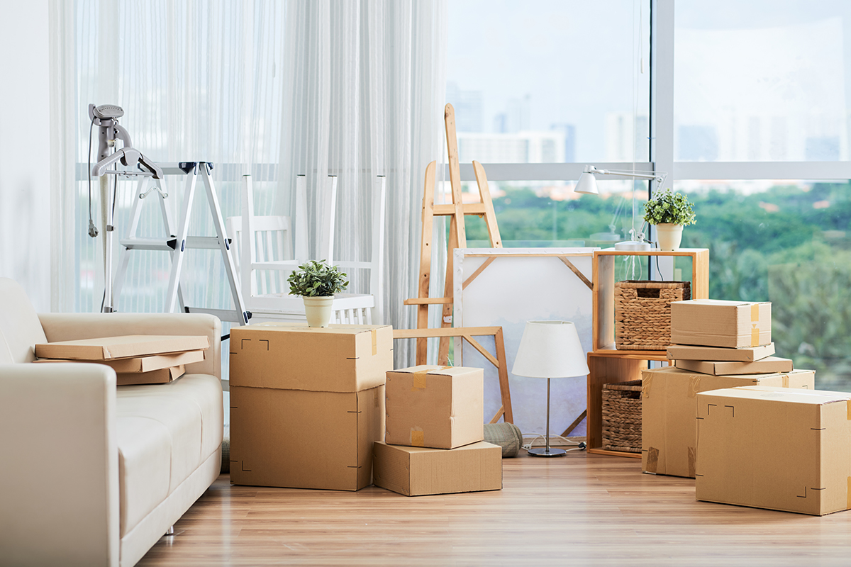 Spacious interior with large packed carton boxed for moving on floor with sofa and drawing easels nearby at large glass wall on sunny day