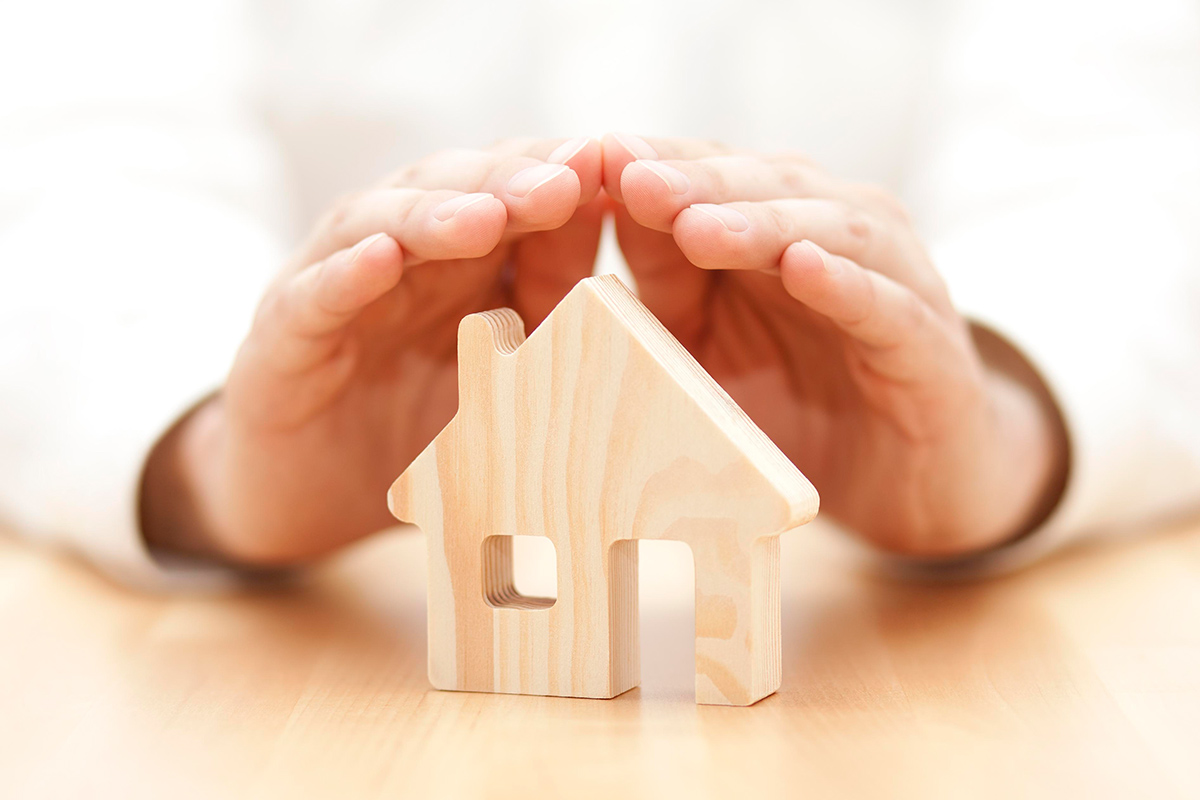 Wooden house model with hands over top protecting