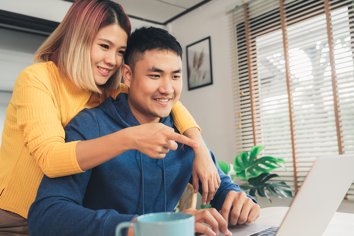 Woman looking and pointing at computer while over man's shoulder