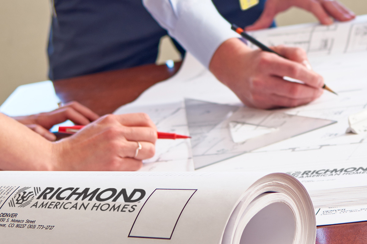 Image of architects marking blueprint on table with pencil and red marker.