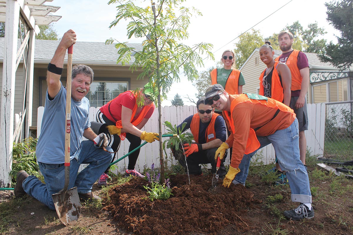 Several people doing community service - smiling around tree they planted and watering it