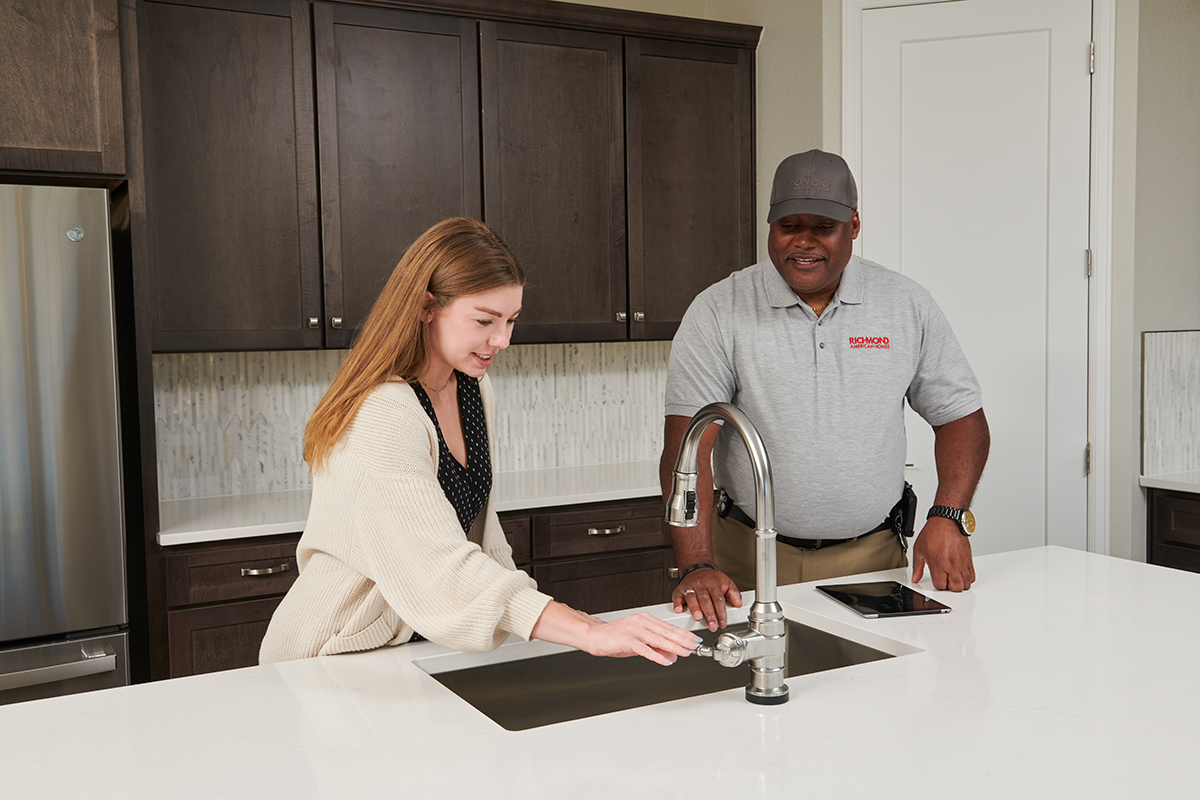 Homeowner turning on sink in kitchen with warranty technician