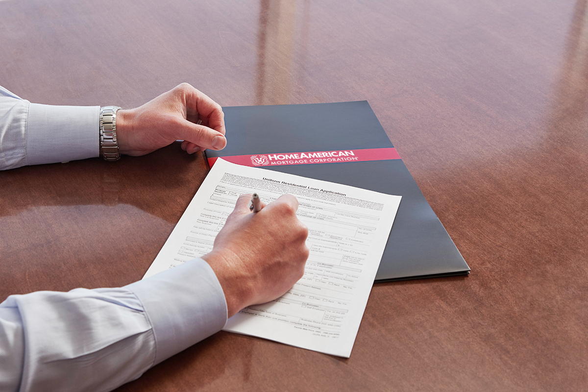 Hand filling out form next to HomeAmerican Mortgage Corporation folder on table
