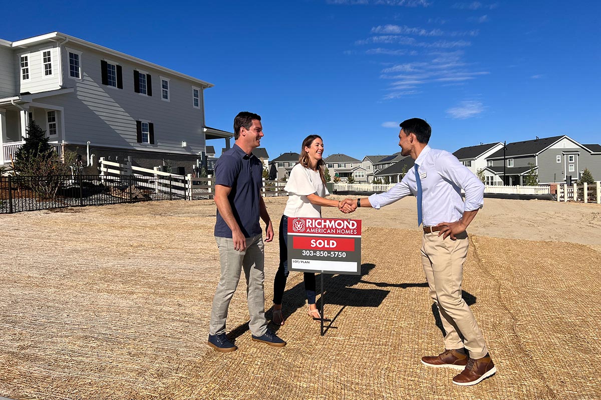 Couple shaking hands with sales associate in front of sold sign on empty lot