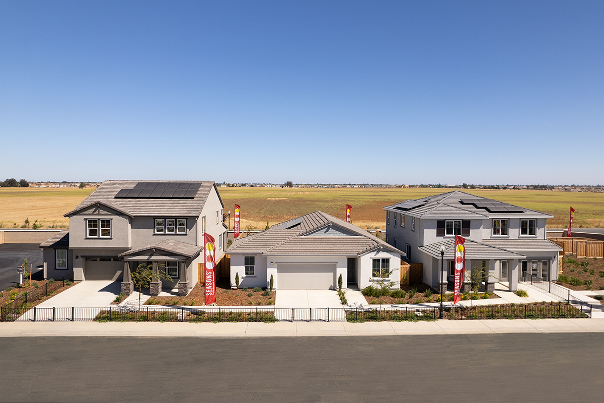 Aerial view of three homes on a street in front of a field with Seasons flags displayed in front of the homes