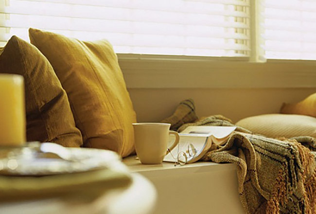 Window seat with pillows, mug, blanket, book, and glasses