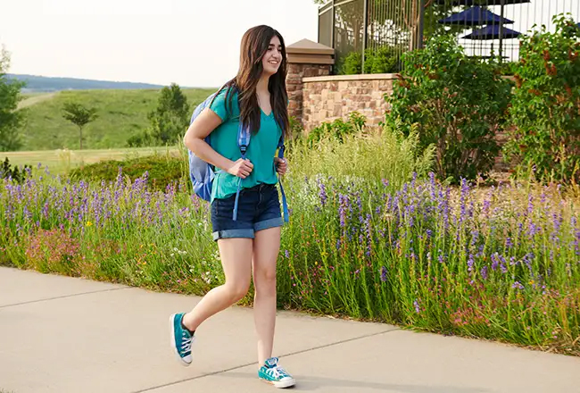 Teenage girl walking on sidewalk with backpack