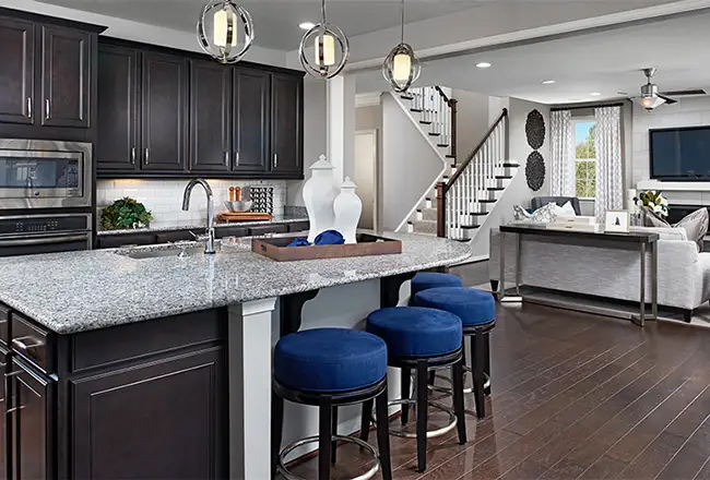 Kitchen with dark cabinets and granite island countertop, with living room and staircase in the background