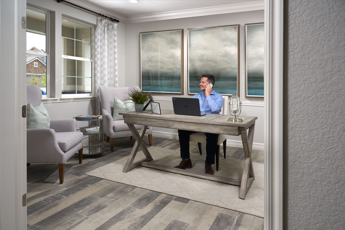 Man sitting at desk in home office talking on his phone while looking out the window