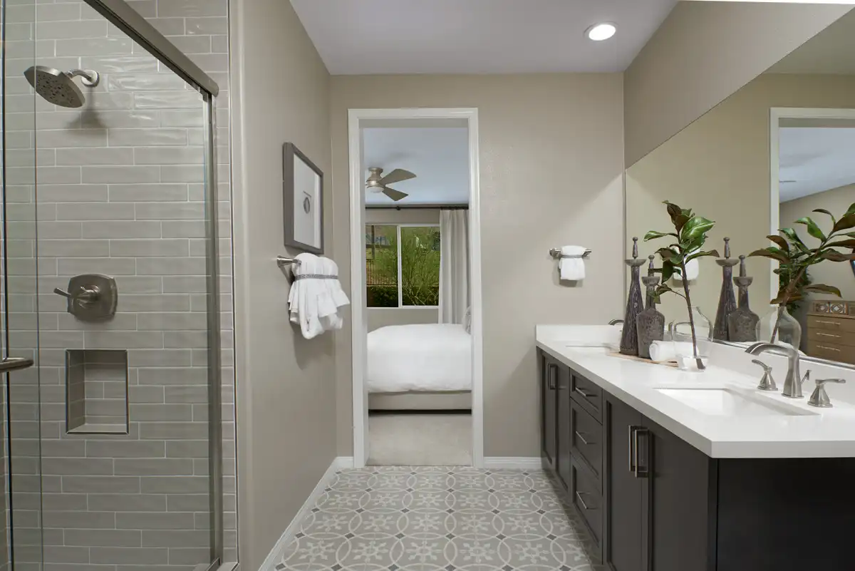 Bathroom with double sink vanity with dark cabinets, patterned floor tile, and a shower stall with brick-patterned tile