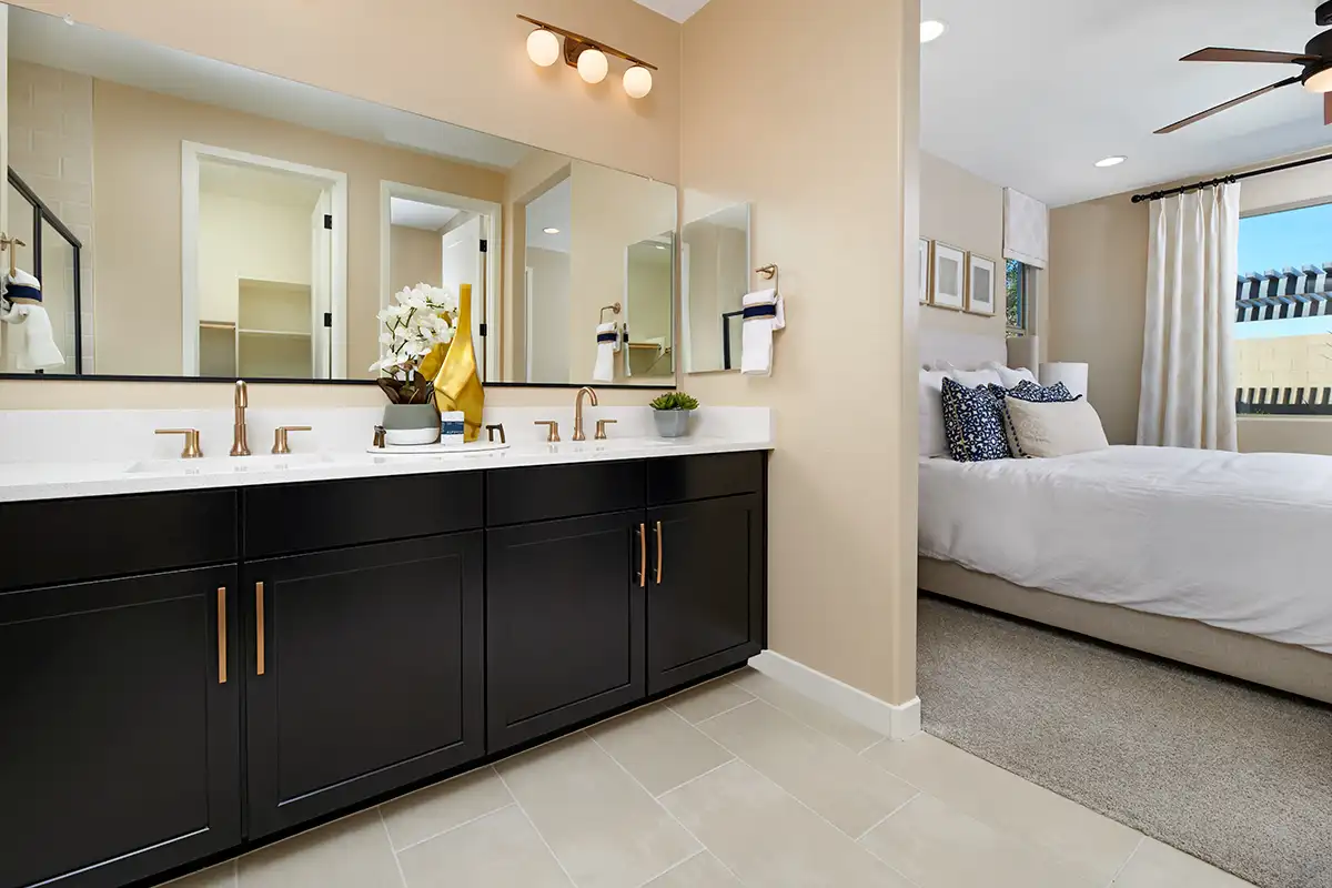Double sink vanity with dark cabinets and gold hardware next to bedroom