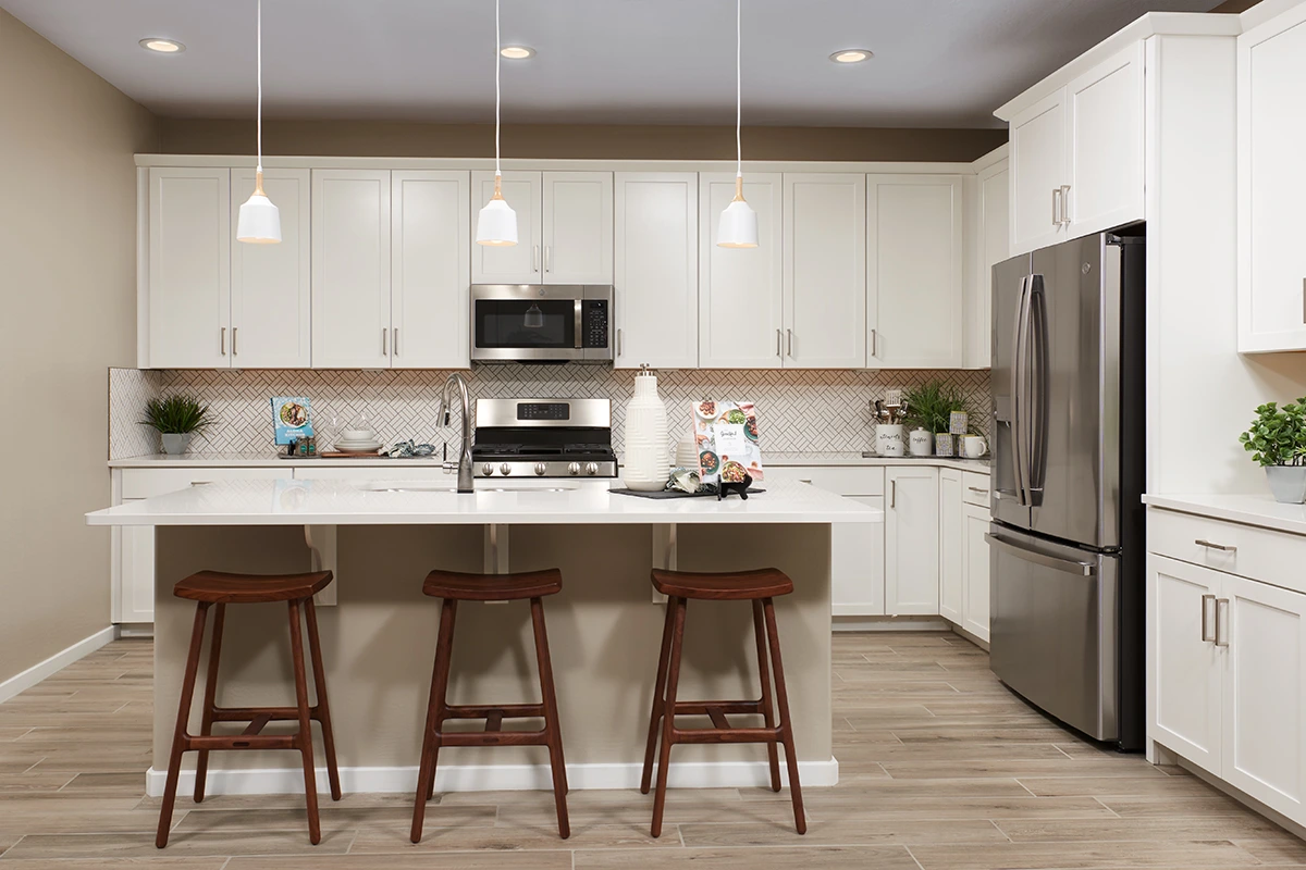 Kitchen with island with three barstools, patterned backsplash, and white cabinets