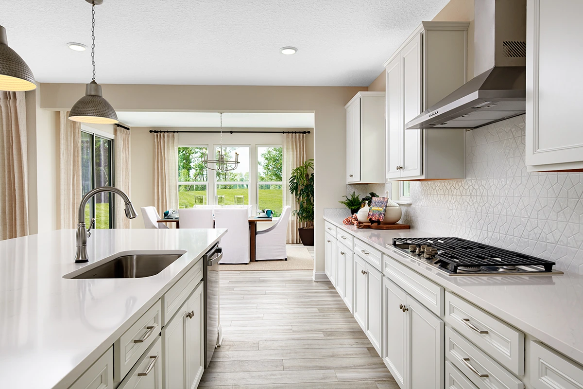 Kitchen with island in front of dining room with sliding doors and three tall windows with tall curtains
